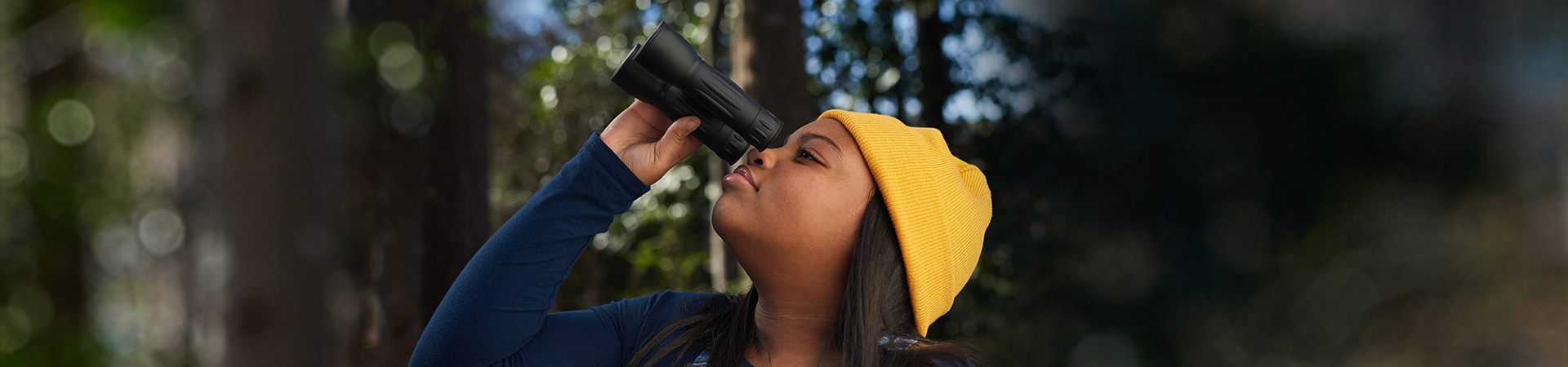  high school girl wearing yellow beanie knitted hat holding binoculars outside in woods 